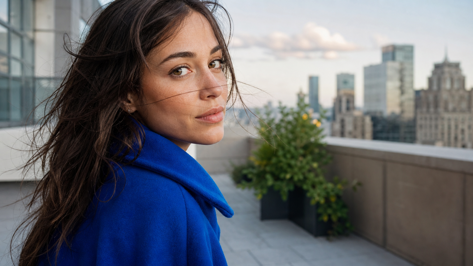 A portrait of a woman in a blue coat turning naturally toward the camera on an urban terrace